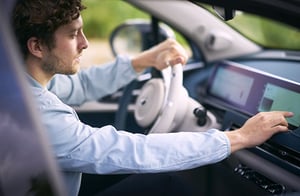 Person sitzt am Steuer eines GWM ORA 03 und bedient den großen Touchscreen auf dem Armaturenbrett; der Innenraum wirkt modern und hell.