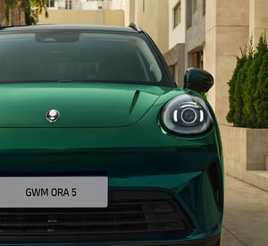 Frontpartie eines grünen GWM ORA 5 in Nahaufnahme mit beleuchtetem LED-Scheinwerfer und Markenlogo auf der Motorhaube.